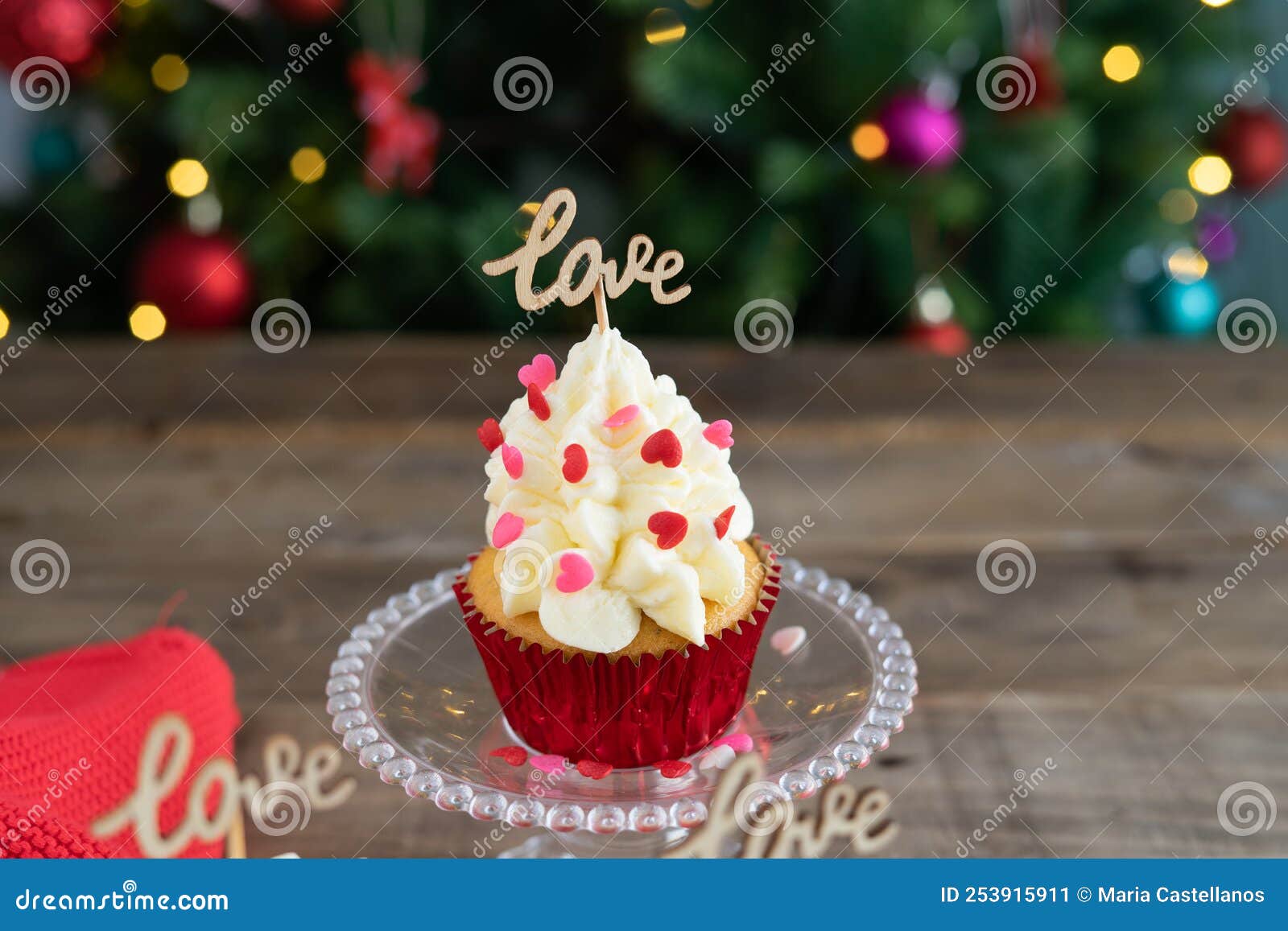 decorated cupcake in display stand on wooden background with love sign and out-of-focus christmas tree in the background. copy