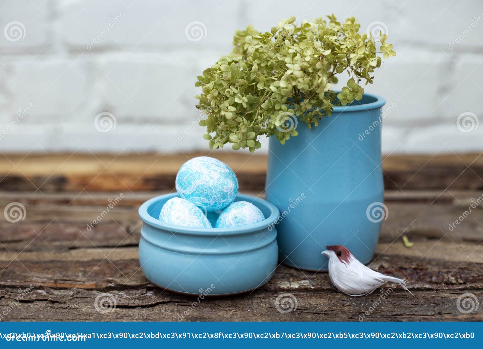 decorative dyed easter eggs in blue pot with green hydrangea in skyey ceramic vasa and a little bird on brown wooden background