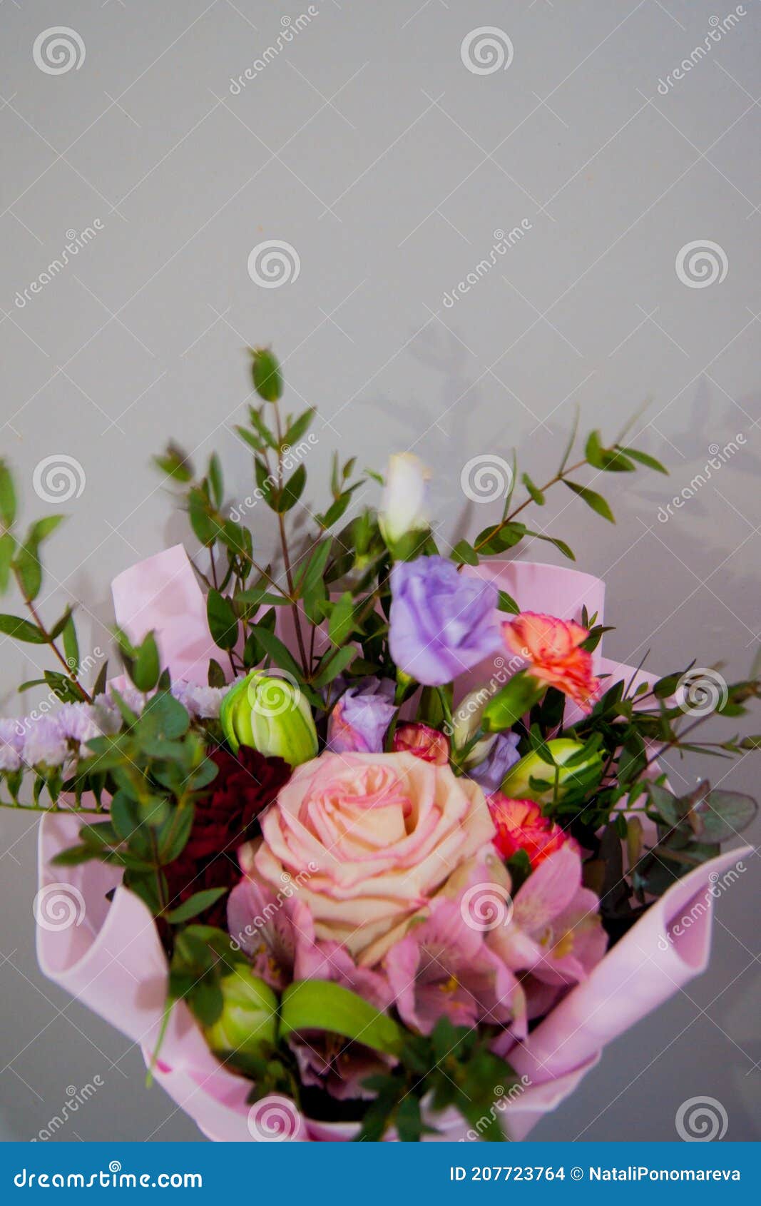 Delicate Bouquet of Different Flowers in a Light Pink Wrapper on a Gray