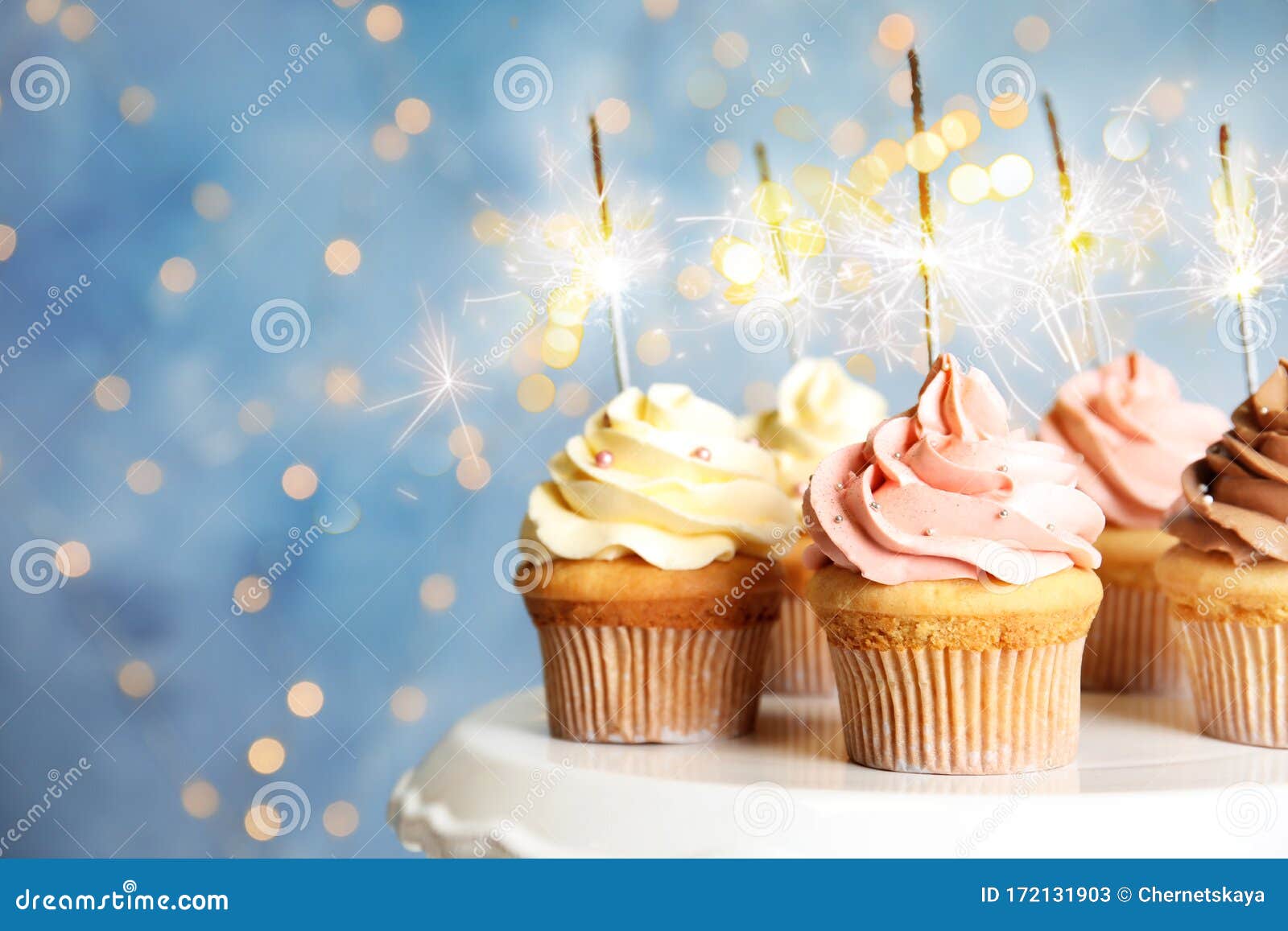 delicious birthday cupcakes with sparklers on stand against blurred background
