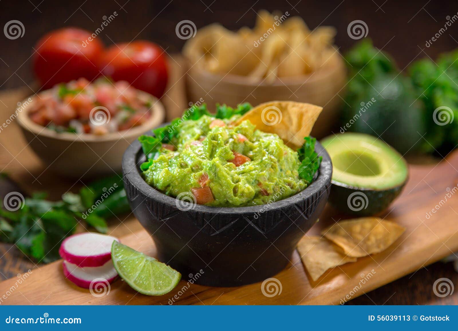a delicious bowl of guacamole next to fresh ingredients on a table with tortilla chips and salsa