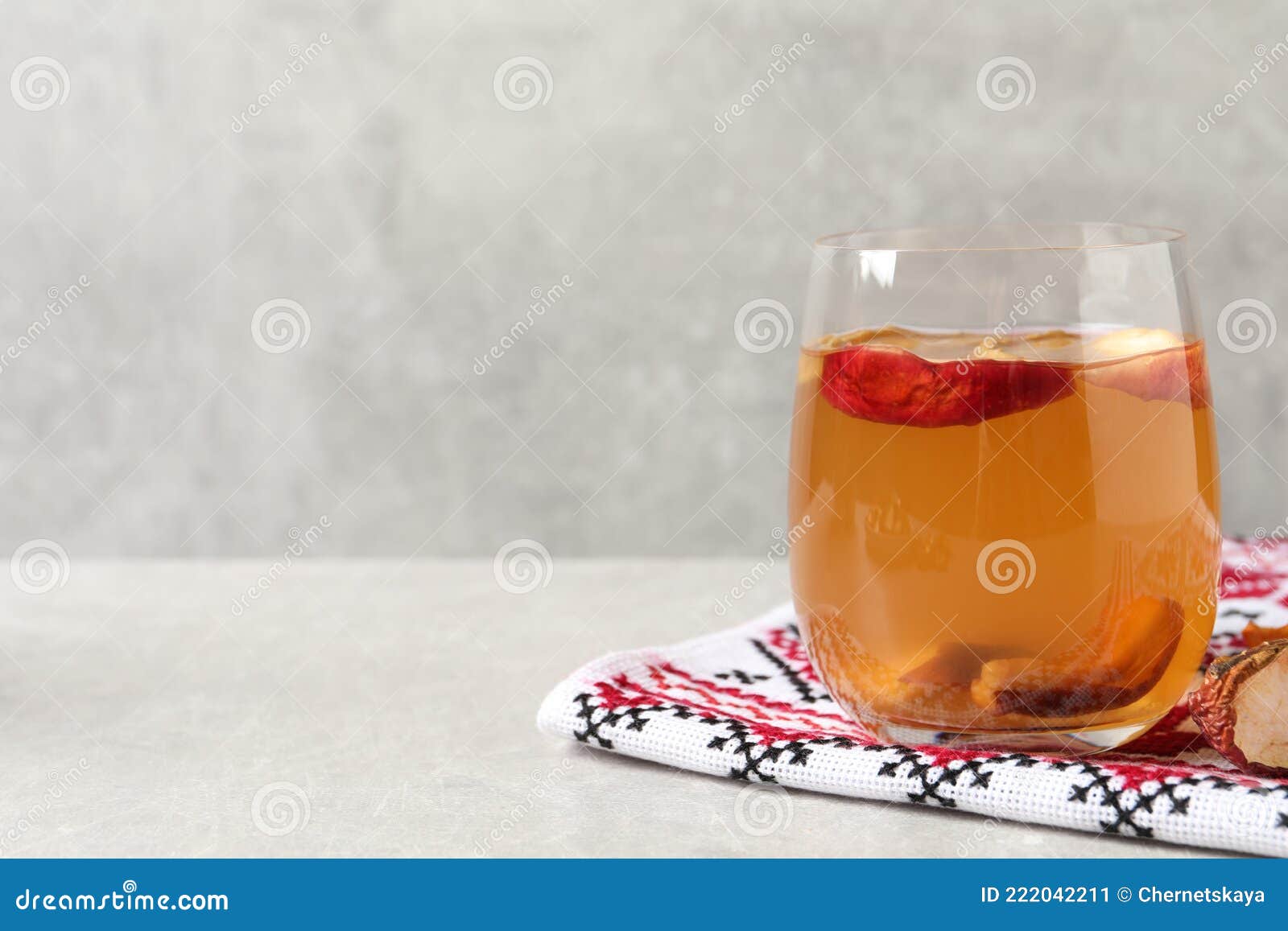 delicious compote with dried apple slices in glass and rushnyk on light grey table, space for text