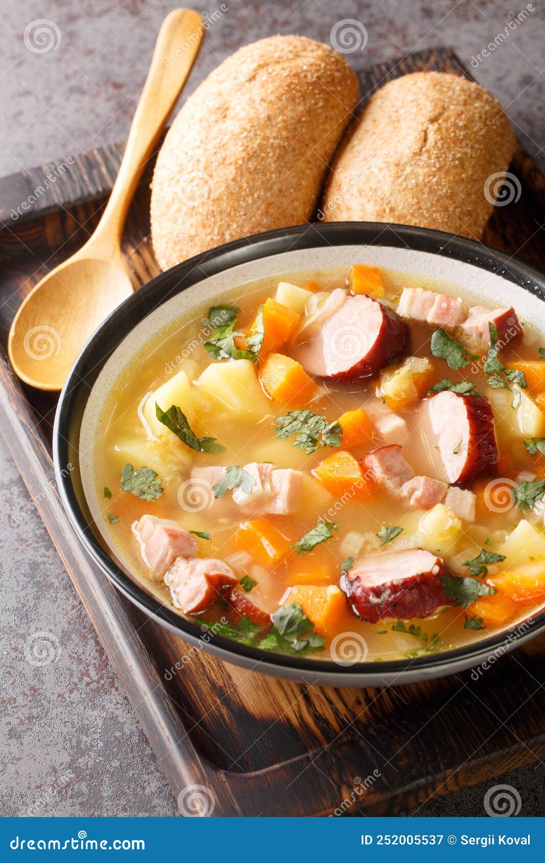 delicious pea soup with vegetables, bacon and sausages close-up in a bowl. vertical