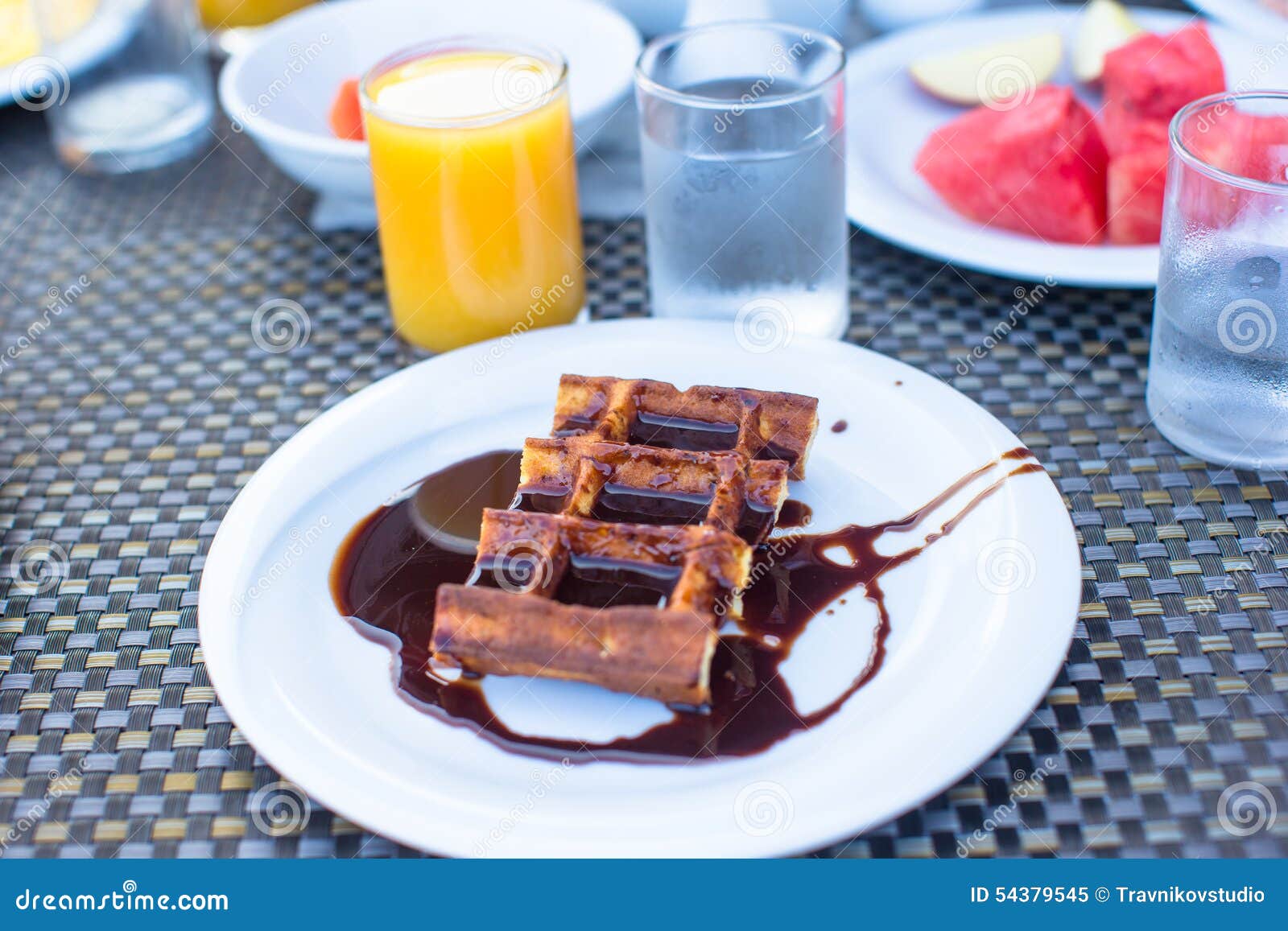 Delicious waffles with chocolate, water and juice. Delicious waffles, cake, coffee and juice served for breakfast at outdoor restaurant