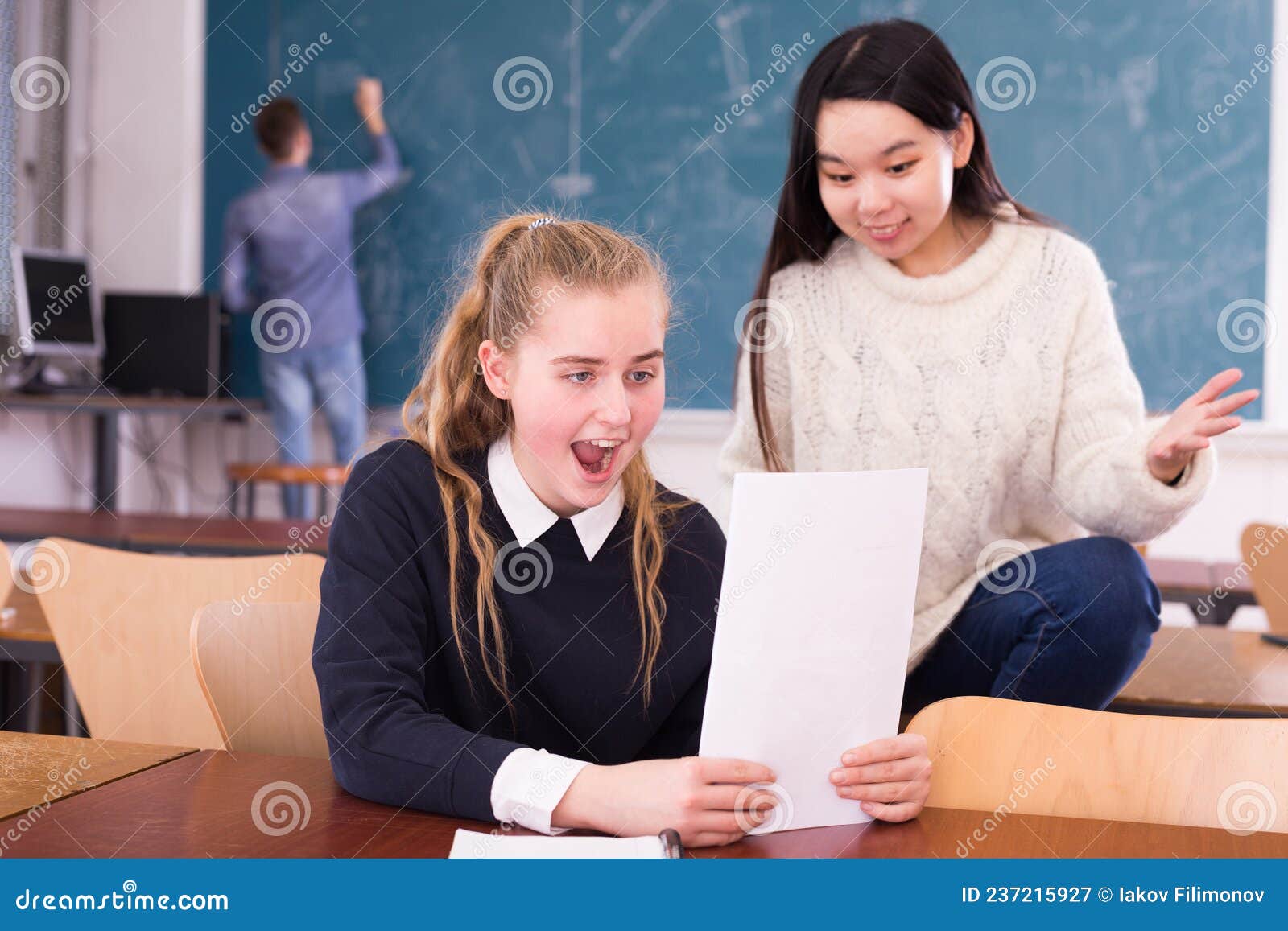 delighted schoolgirl and chinese girl schoolmate reading notification