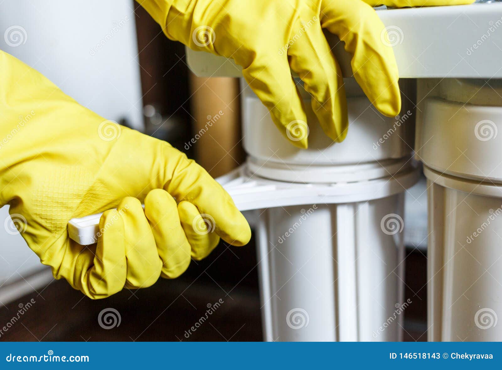 Close up Plumber in yellow household gloves changes water filters. Repairman changing water filter cartridges in kitchen. Drinkable water filtration system in the kitchen. Clean water at home