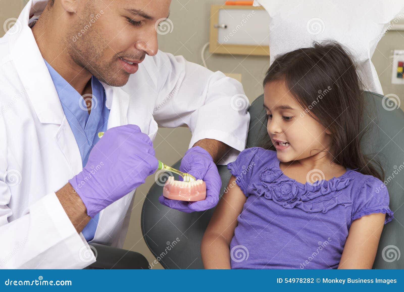 dentist demonstrating how to brush teeth to young female patient