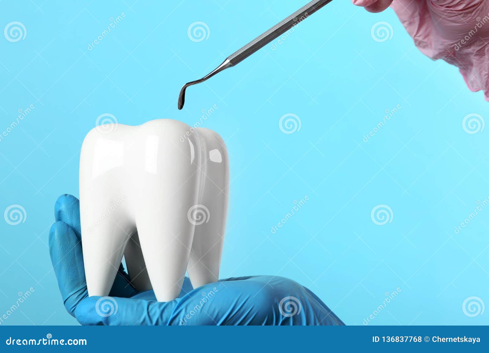 dentist holding ceramic model of tooth and professional tool on color background
