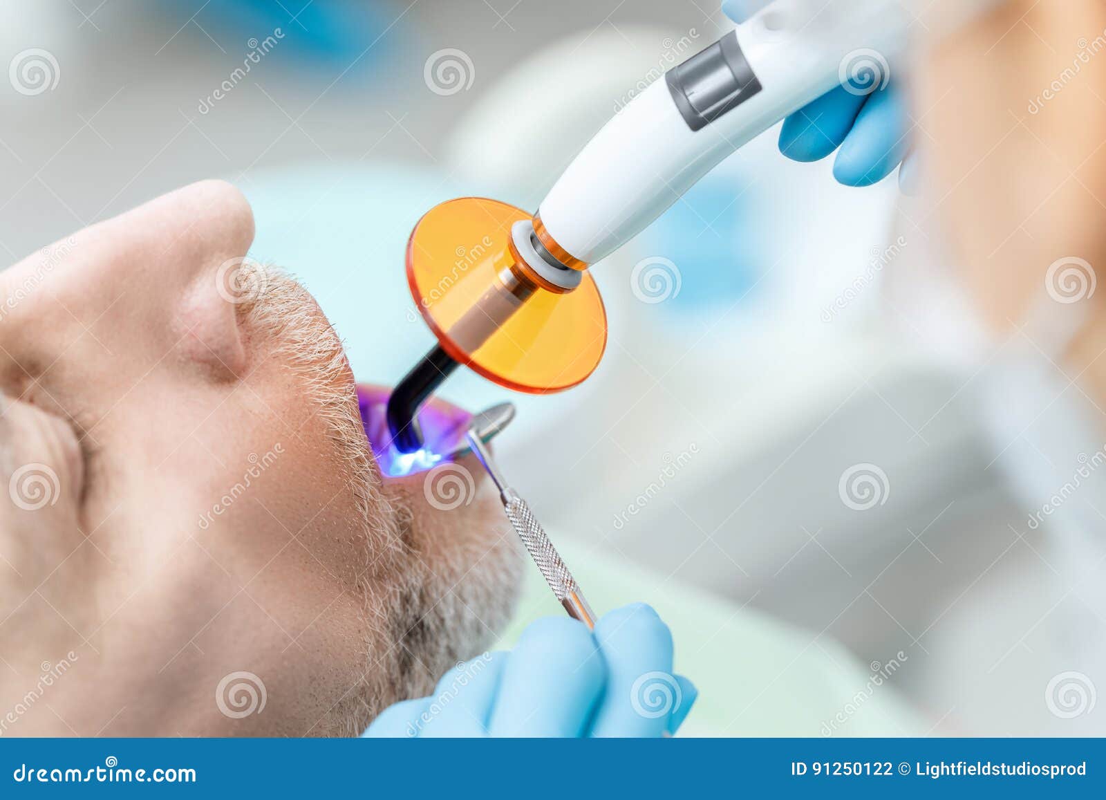 Dentist Using Dental Curing UV Lamp on Teeth of Patient Stock Photo