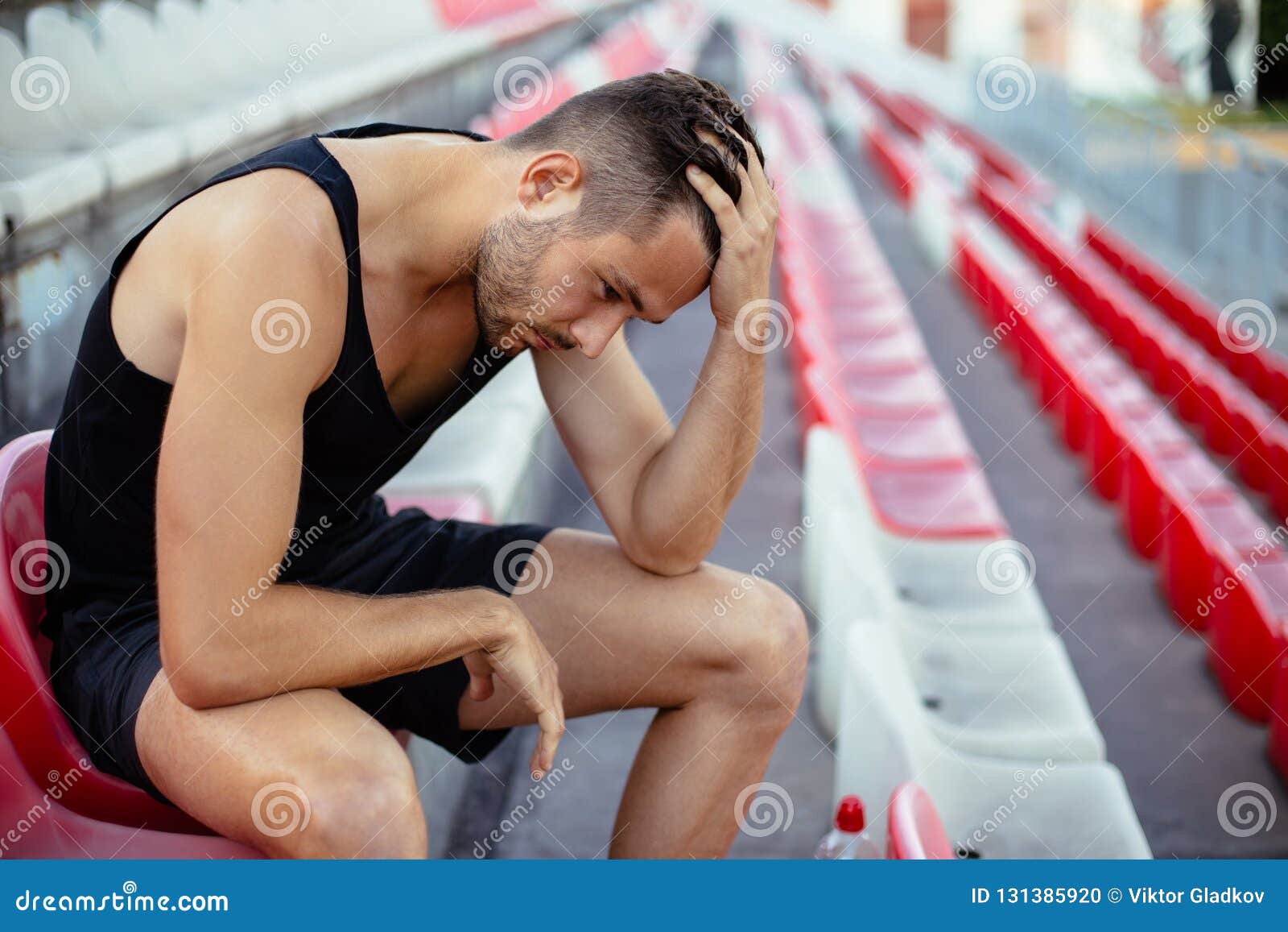 depressed athlete man sitting head in hands on stadium seats