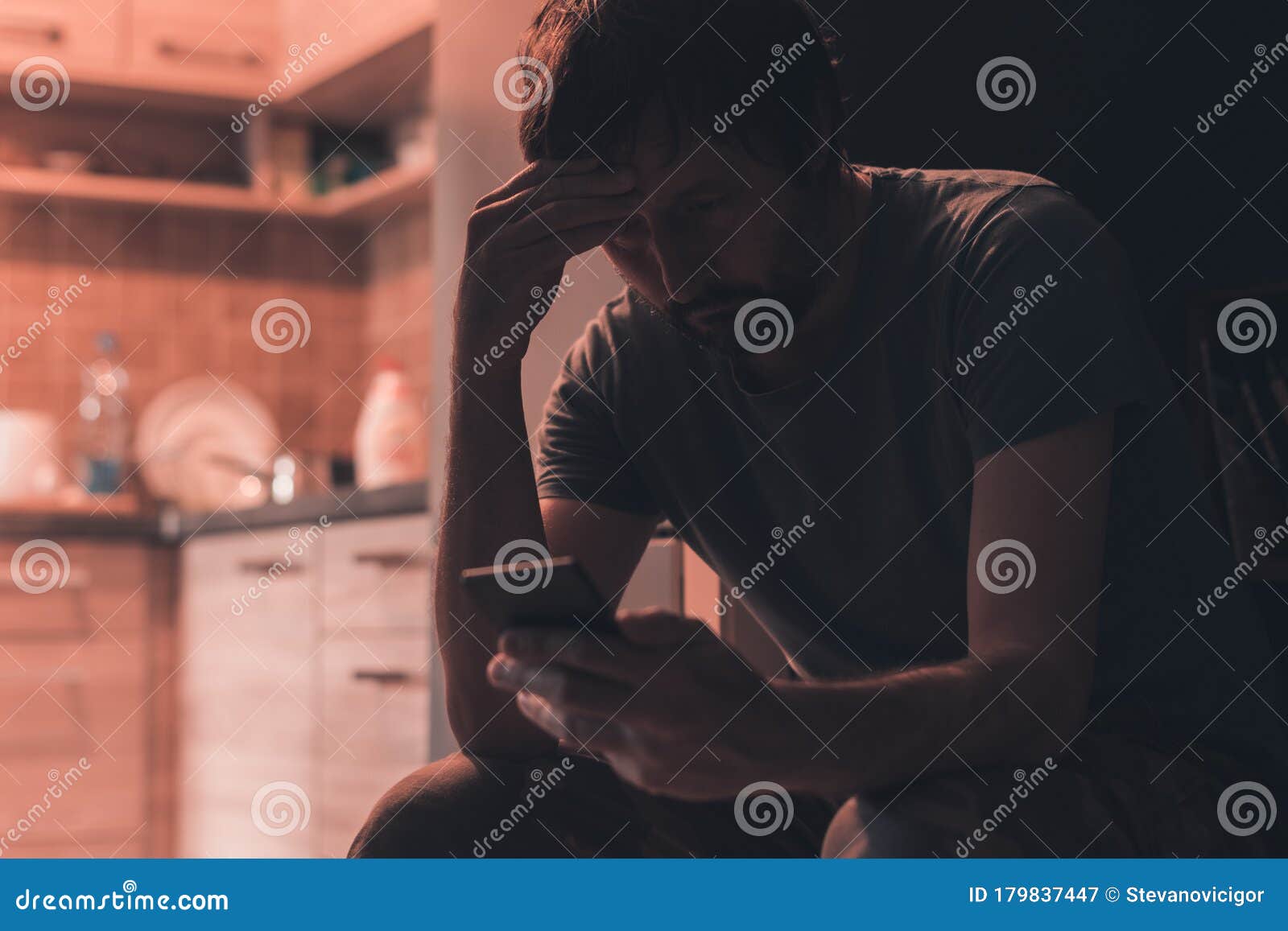 depressed man typing text message on mobile phone in dark room