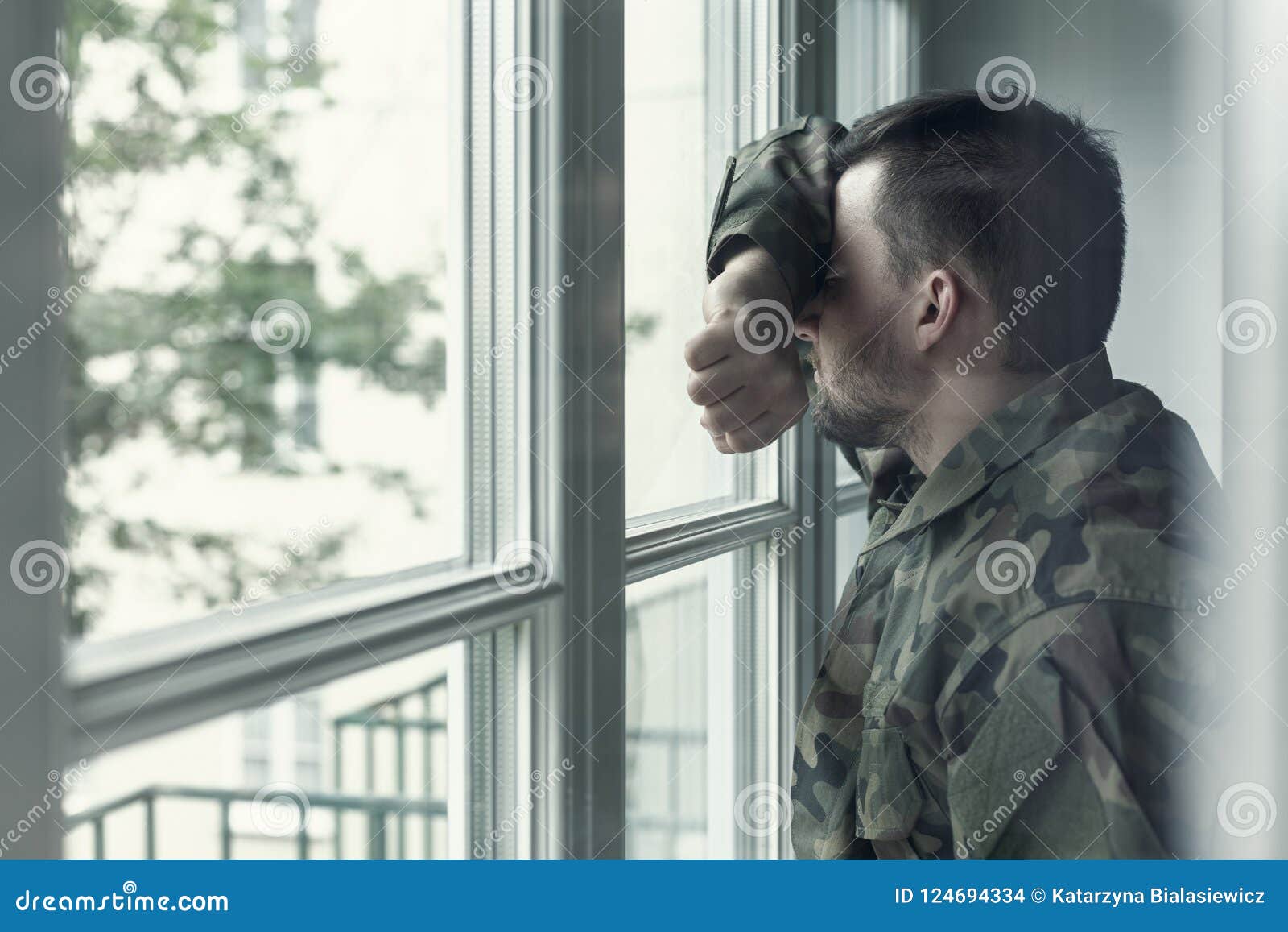 depressed and sad soldier in green uniform with trauma after war standing near the window