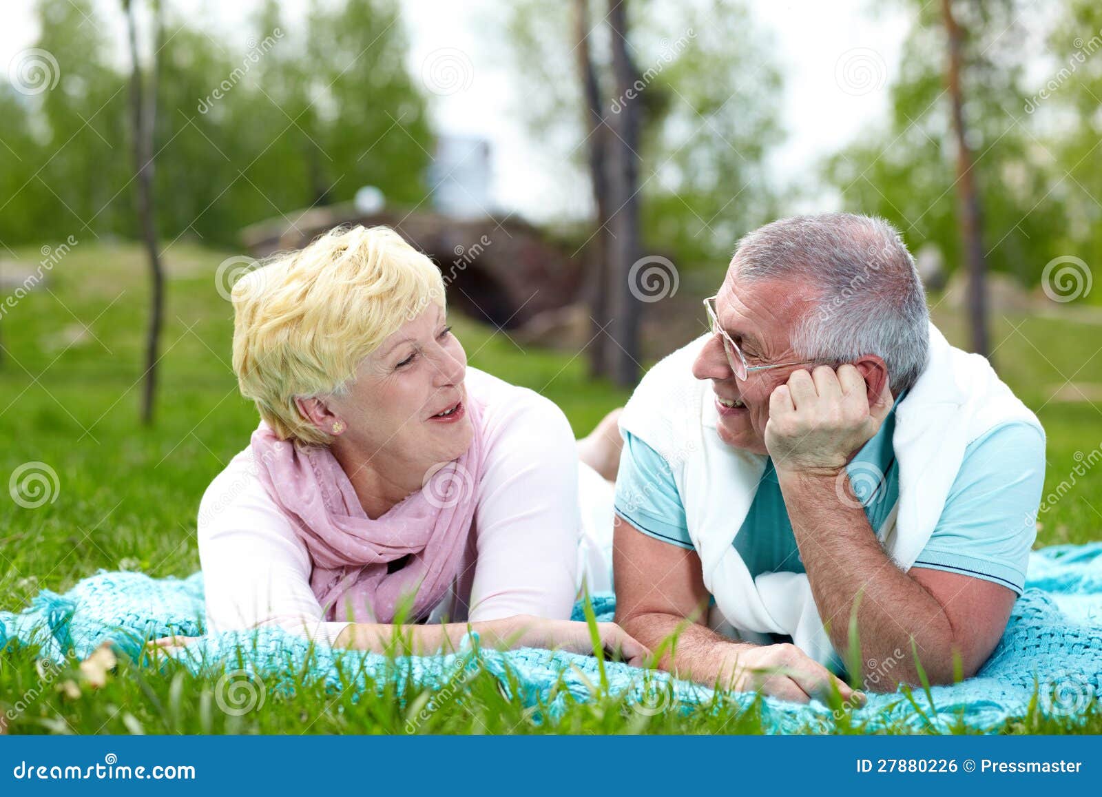 Glückliche reife Paare, die auf Gras liegen und in der Landschaft sprechen