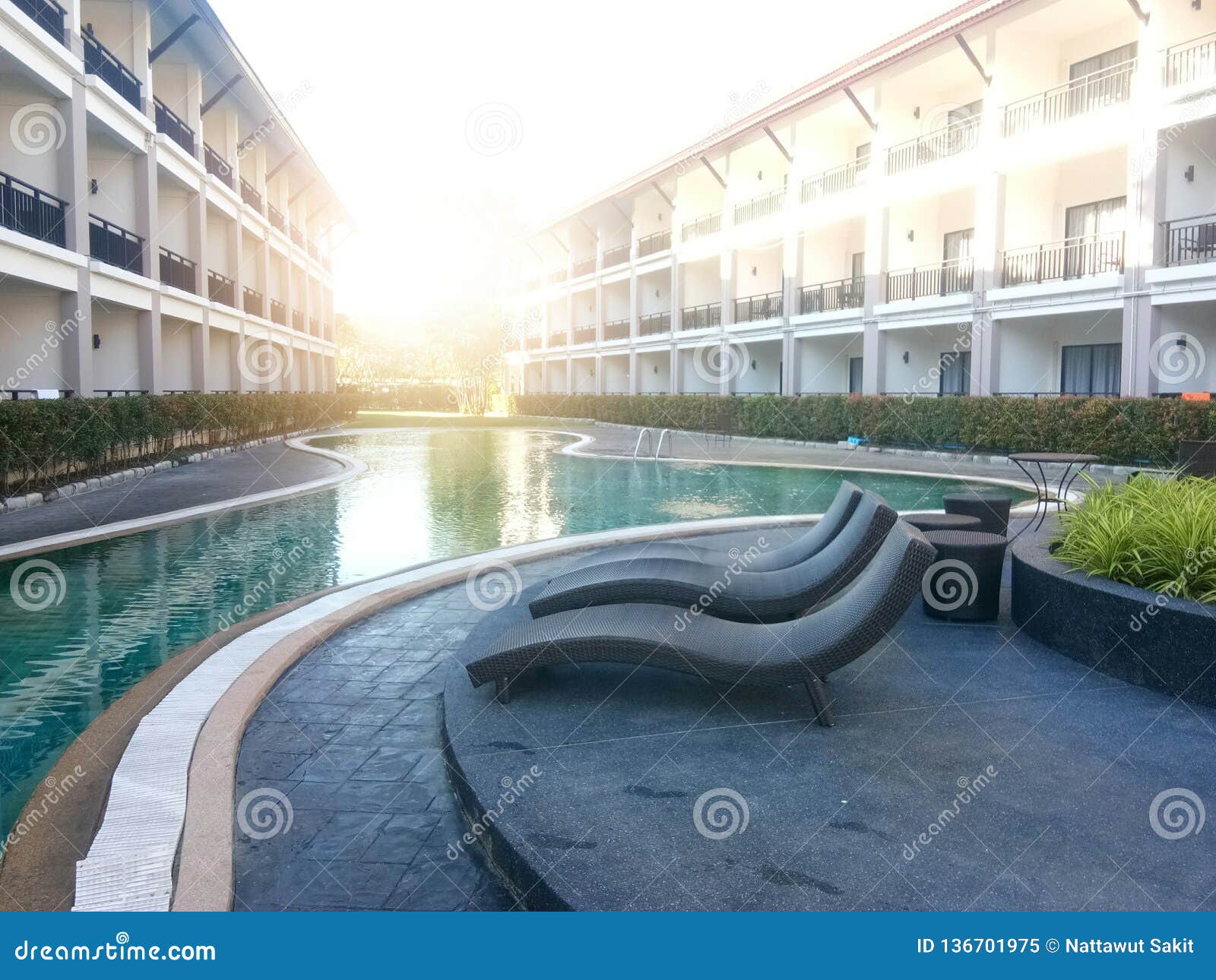 Der Swimmingpool ist zwischen dem Gebäude und dem orange Licht der Sonne morgens Am Rand des Pools, gibt es einen Sitz, der für die Entspannung vereinbart wird Klares Wasser macht die Reflexion vom Gebäude