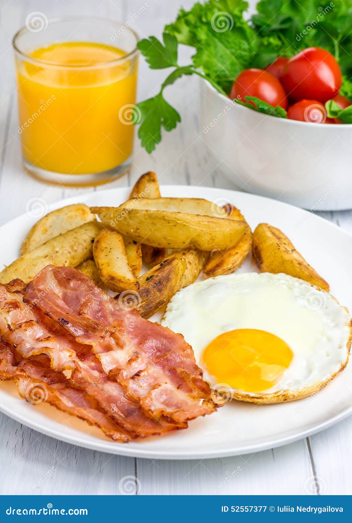 Desayuno caluroso con tocino, el huevo frito, la patata y el vidrio de zumo de naranja