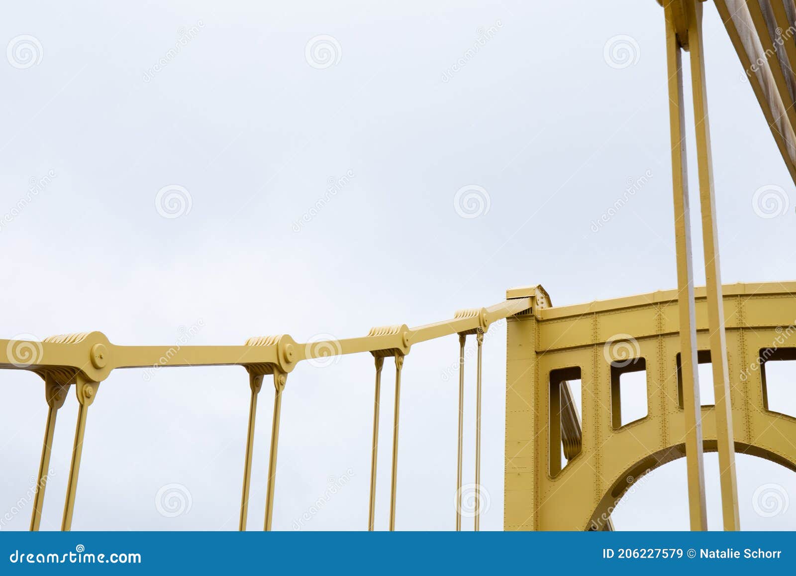 detail of a self anchored suspension bridge painted yellow silhouetted against a pale gray sky