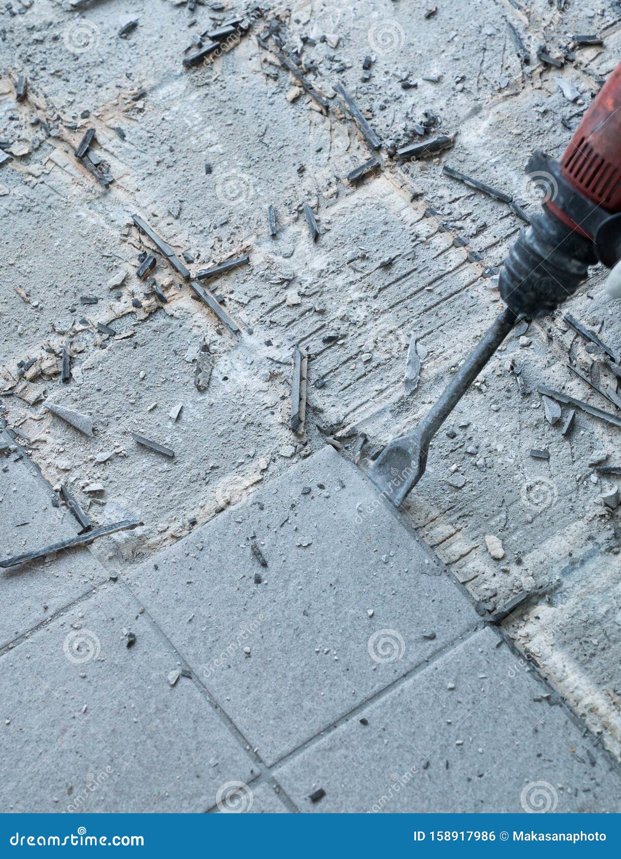 construction worker using a handheld demolition hammer and wall breaker to chip away and remove old floor tiles during renovation