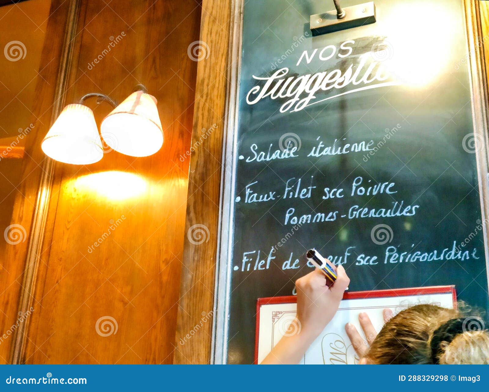 detail of a waitress writing the menu of the day in a board inside a bistrot, paris, france