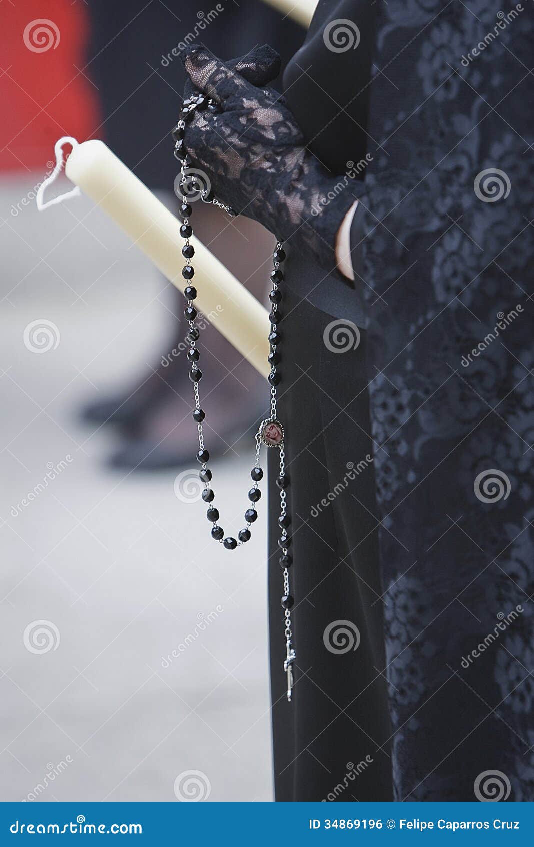 detail of a woman dressed in mantilla holding a rosary and a candle during a holy week procession