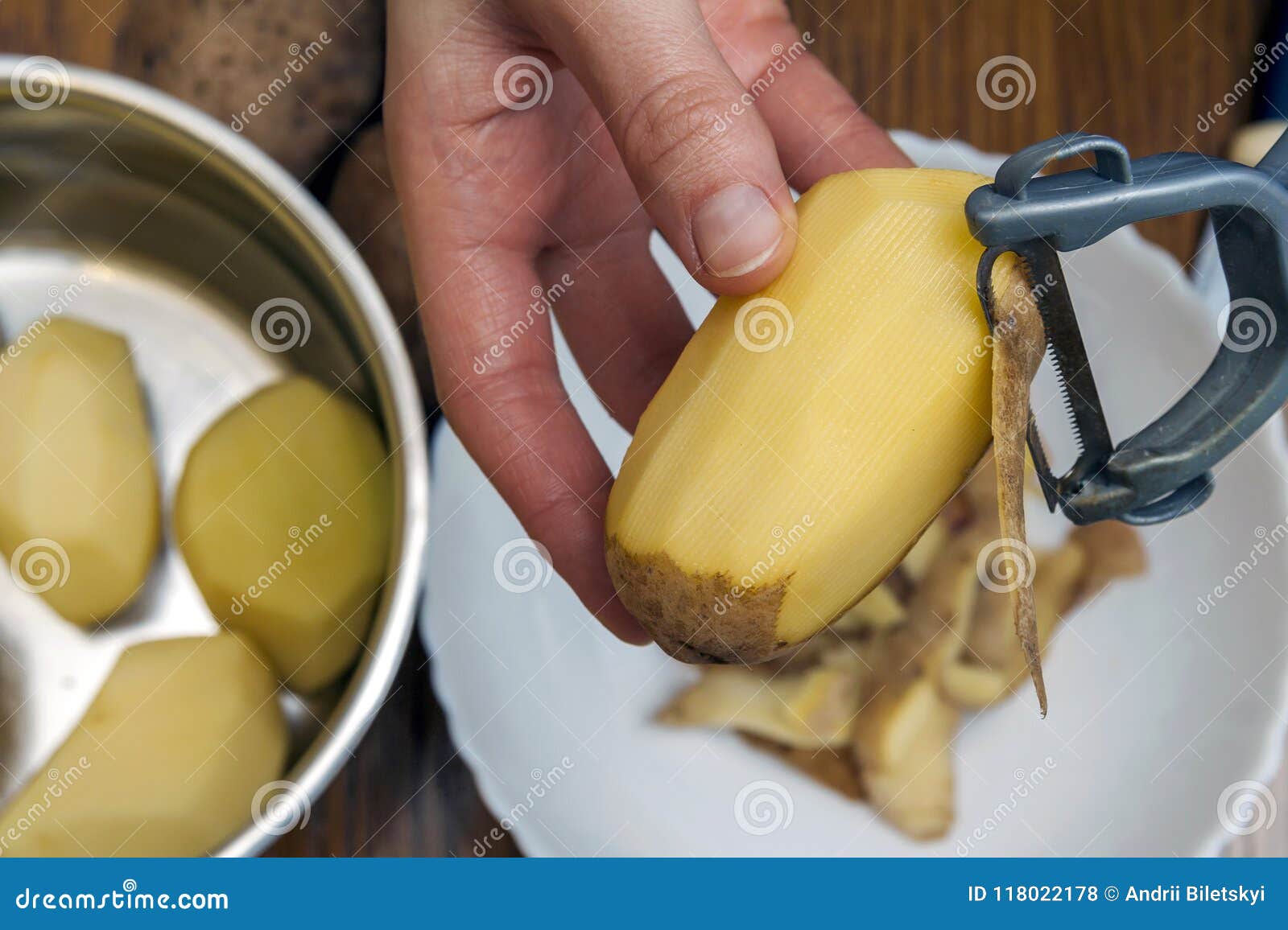 detail of woman hands peeling fresh yellow potato with kitchen p