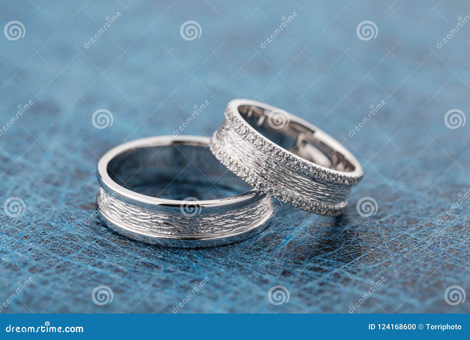 Deux anneaux de noces d'argent texturisés sur le fond bleu. Deux ont donné à des anneaux une consistance rugueuse de noces d'argent avec des diamants sur le fond bleu Anneaux d'or blanc avec des gemmes