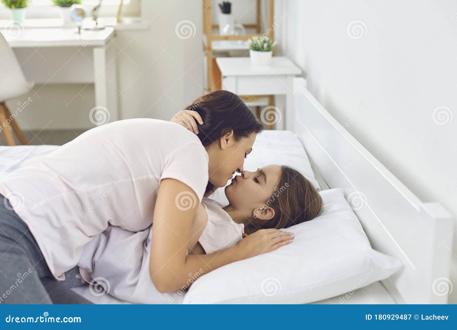Dia Das Mães Felizes. Mãe Abraça a Filha Dando Um Beijo Deitada Numa Cama Branca De Manhã Em