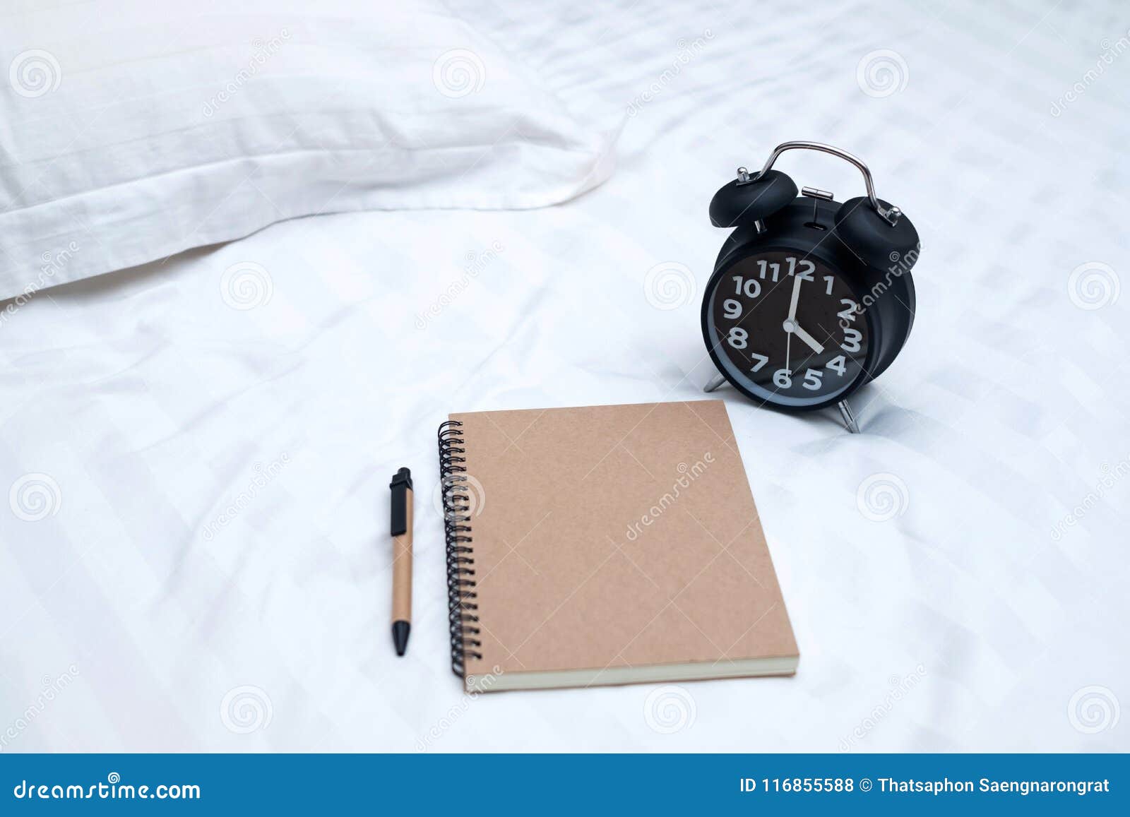Diary or Notebook and Vintage Alarm Clock on Bed in Bedroom at H Stock