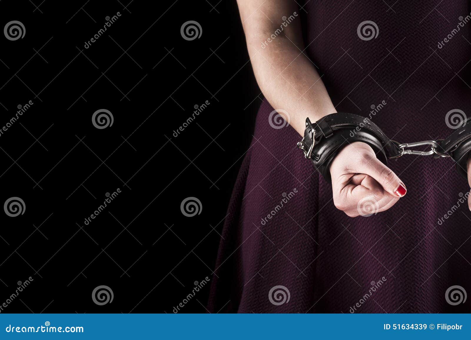 Die gefügige Frau, die ein purpurrotes Kleid im Leder trägt, fesselt an mit Handschellen. Gefügige Frau, die ein purpurrotes Kleid in den ledernen Handschellen trägt