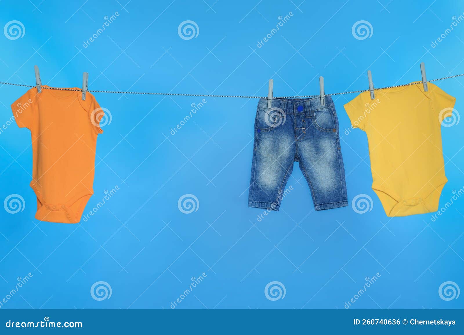 Different Baby Clothes Drying on Laundry Line Against Light Blue