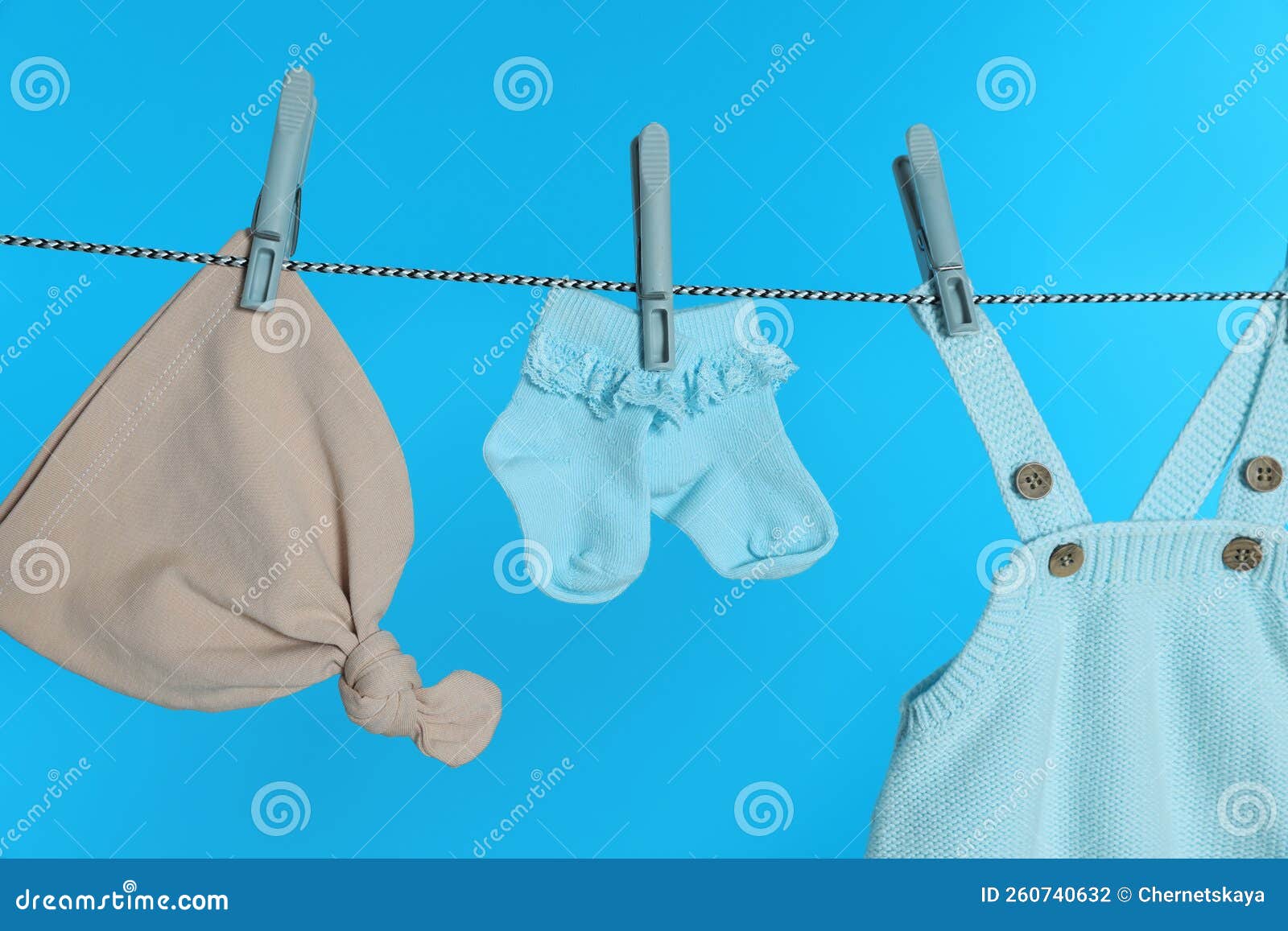 Different Baby Clothes Drying on Laundry Line Against Light Blue