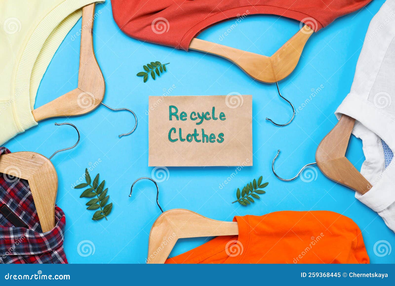 Different Clothes with Recycling Label and Hangers on Light Blue