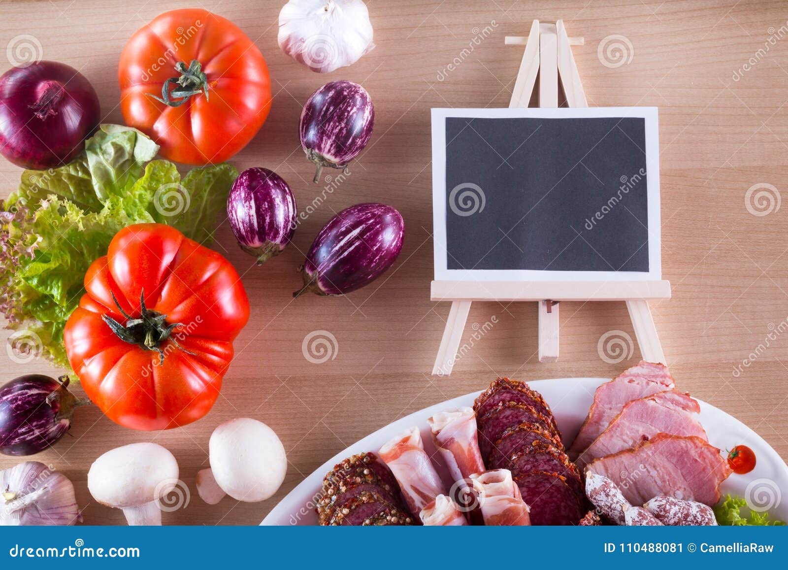 different meat appetizer on plate like jamon, bacon, salami with different vegetables and copy space on blackboard.