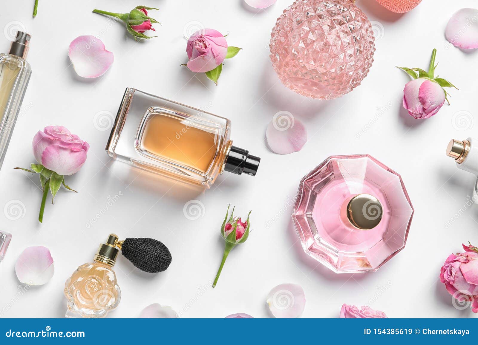 different perfume bottles and flowers on white, top view