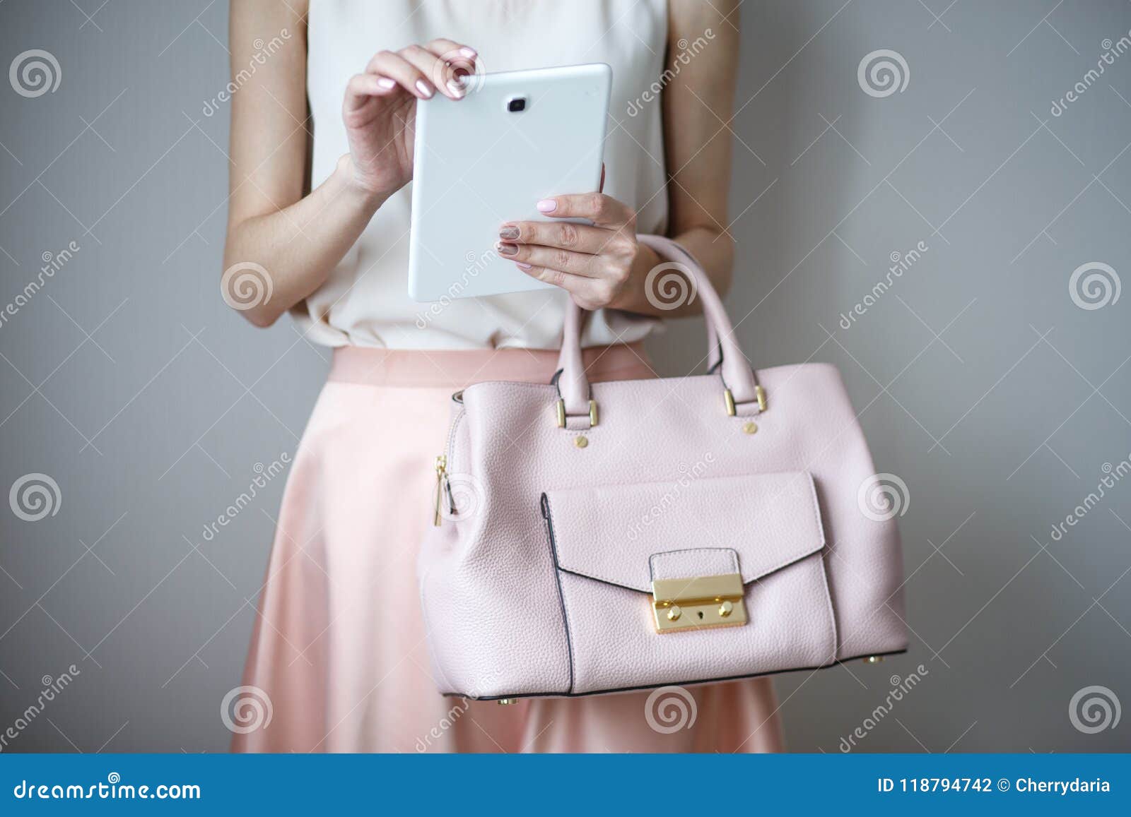 digital electronic tablet on a woman`s hands. leather light pink handbag, summer elegant style