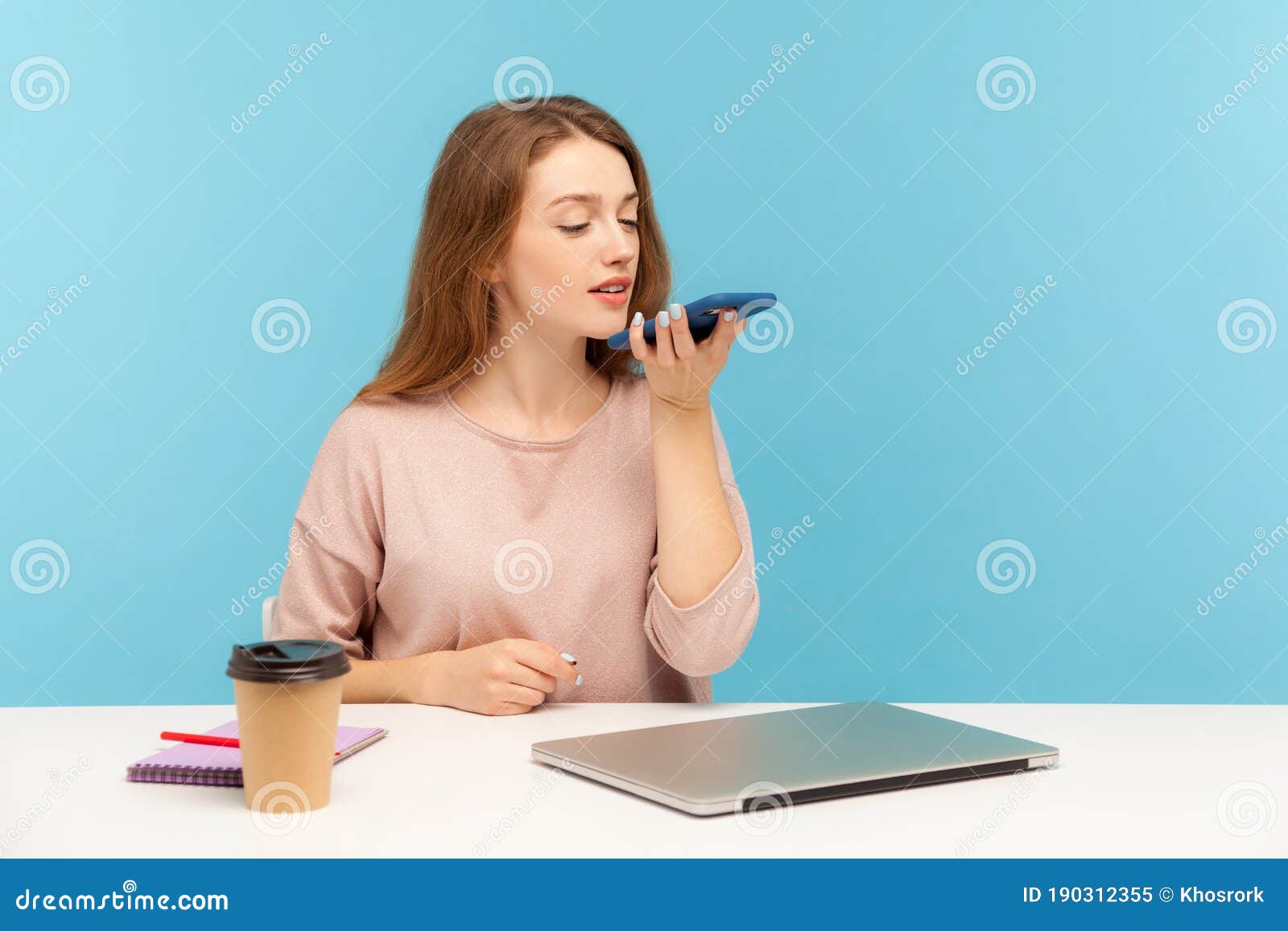 digital speaker app. young woman employee sitting at workplace and talking to mobile phone, using voice assistant