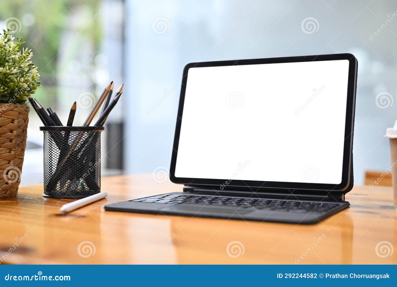 digital tablet, pencil holder and houseplant on wooden table. white screen for advertising