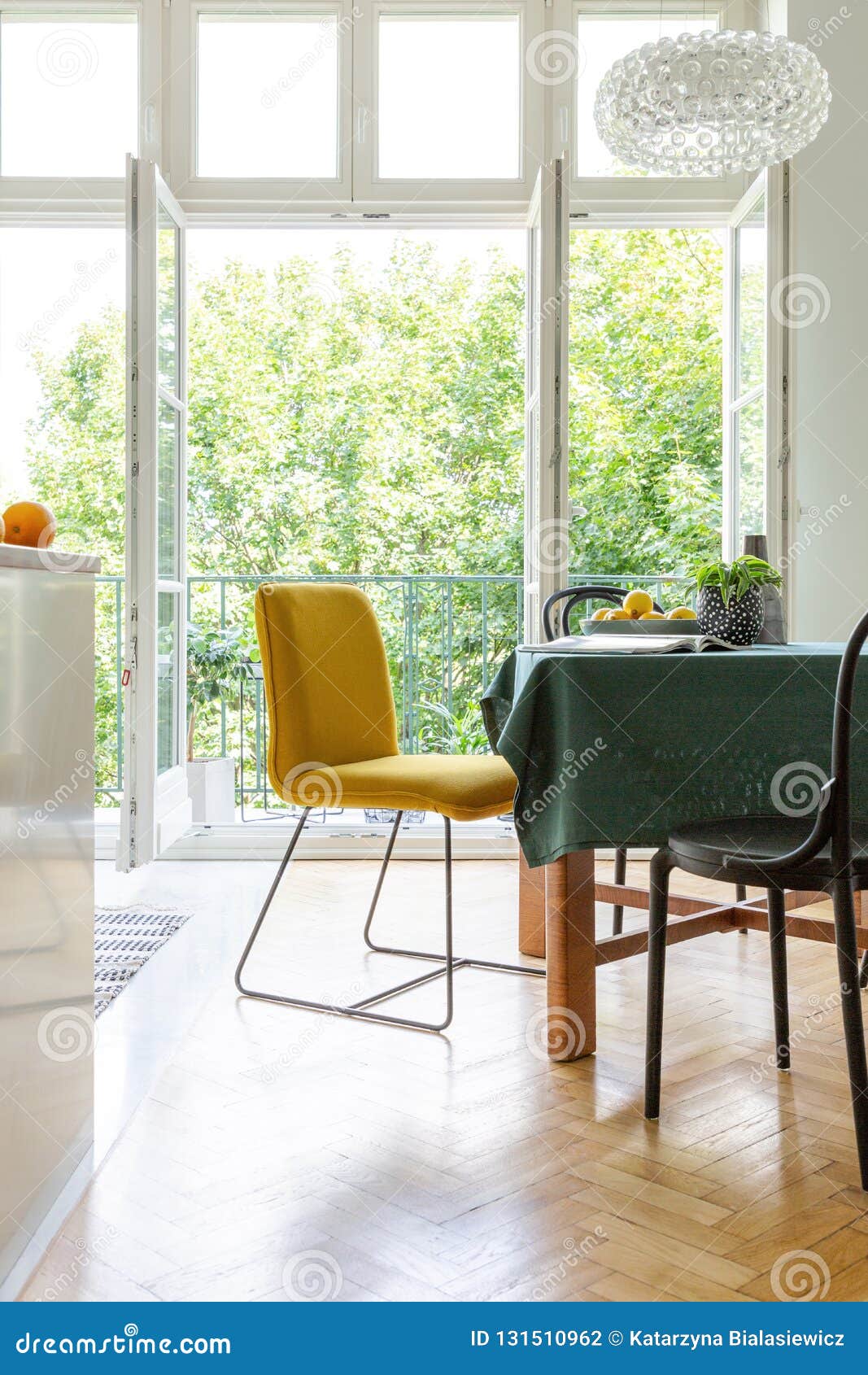 Dining room table with yellow and black chairs , real photo. Vertical view of dining room table with yellow and black chairs and green tablecloth, stylish chandelier above it, real photo