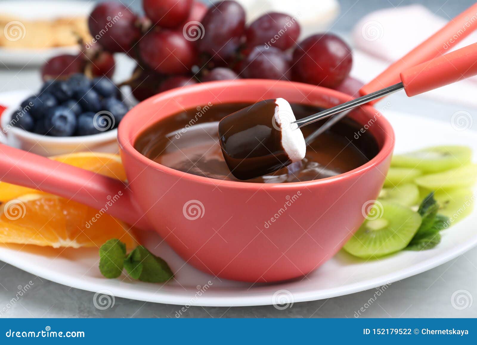 Dipping Marshmallow into Pot with Chocolate Fondue on Table Stock Photo