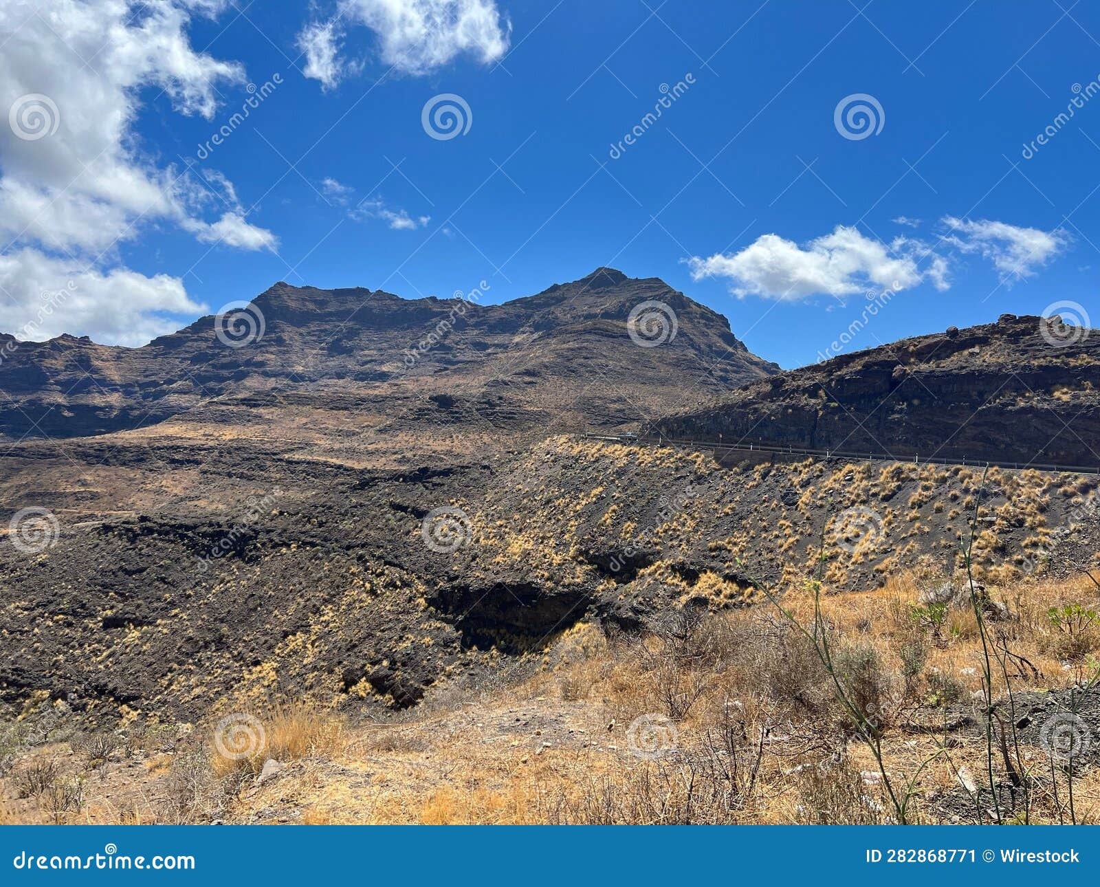 a dirt ground field with some brown grass and mountains in the background