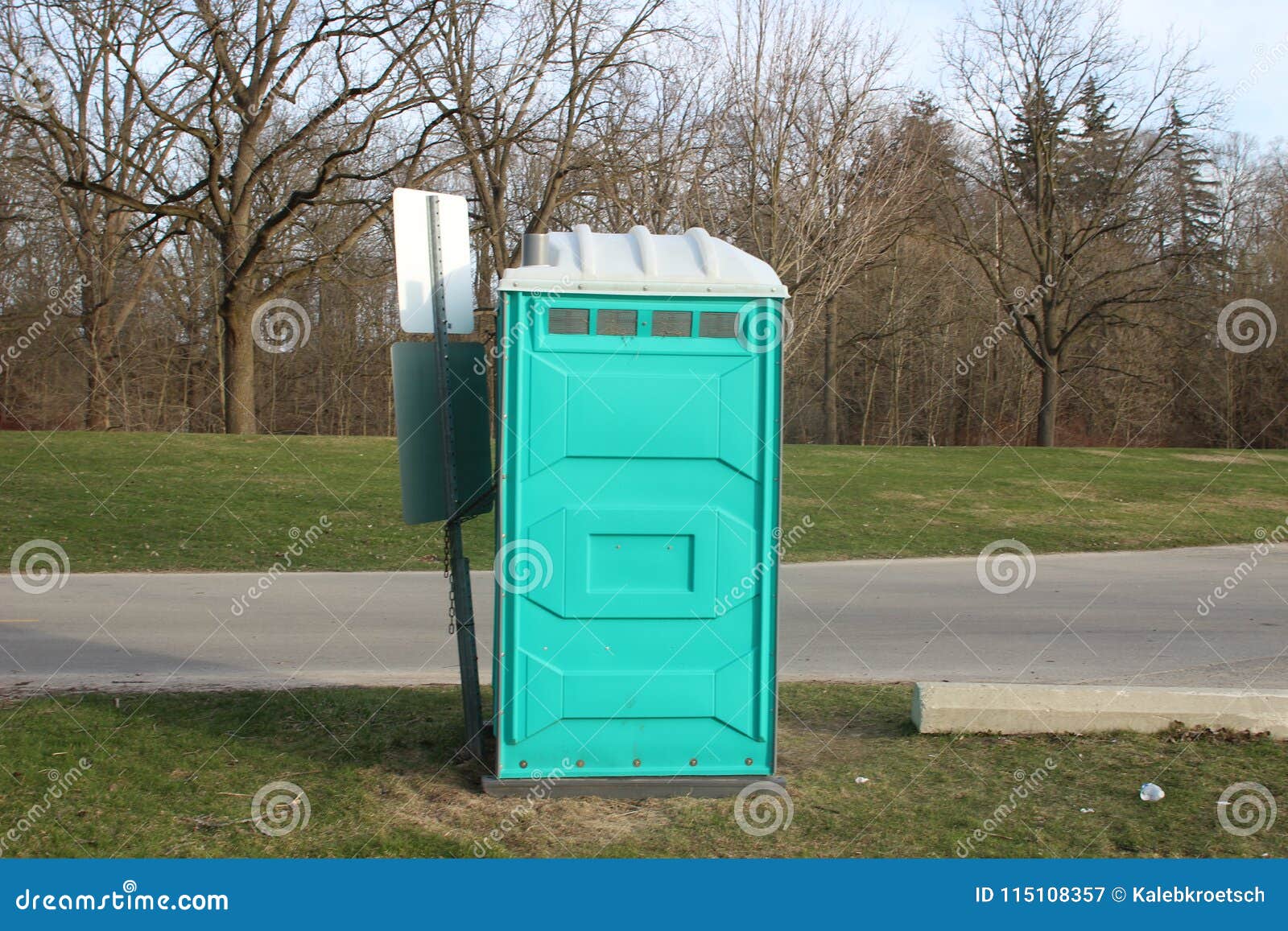 a dirty, blue portable toilet in a park, nasty looking place to go to the bathroom