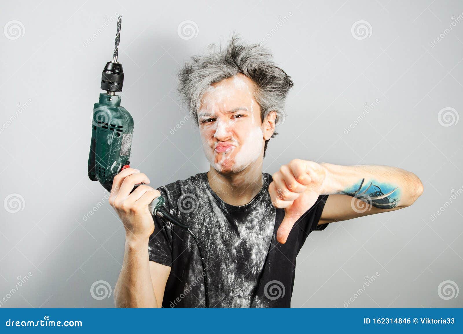 dirty young builder guy in plaster is hold a green drill perforator on gray background at home during repairs