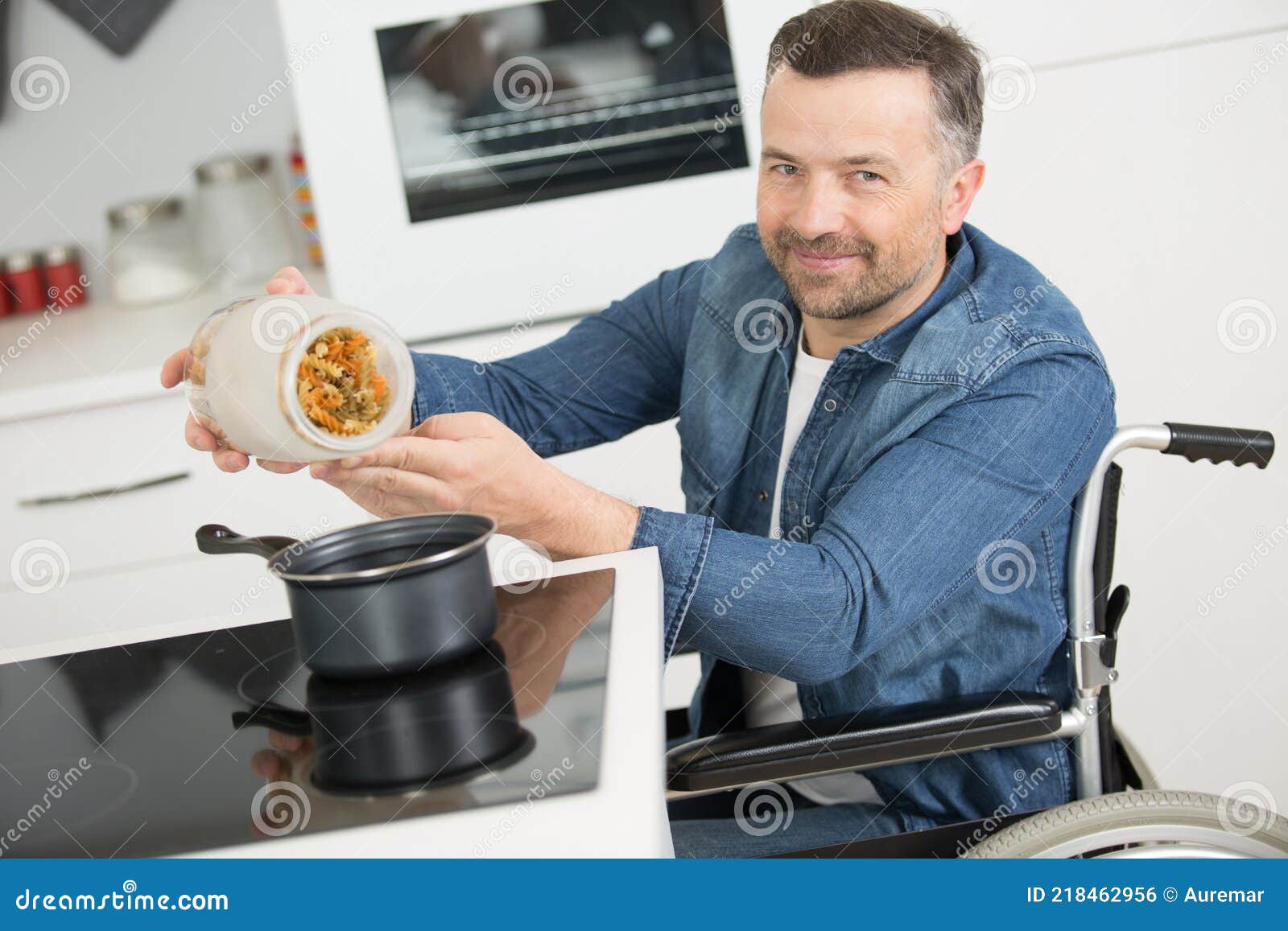 Disabled Young Man in Wheelchair Cooking Meal in Kitchen Stock Photo