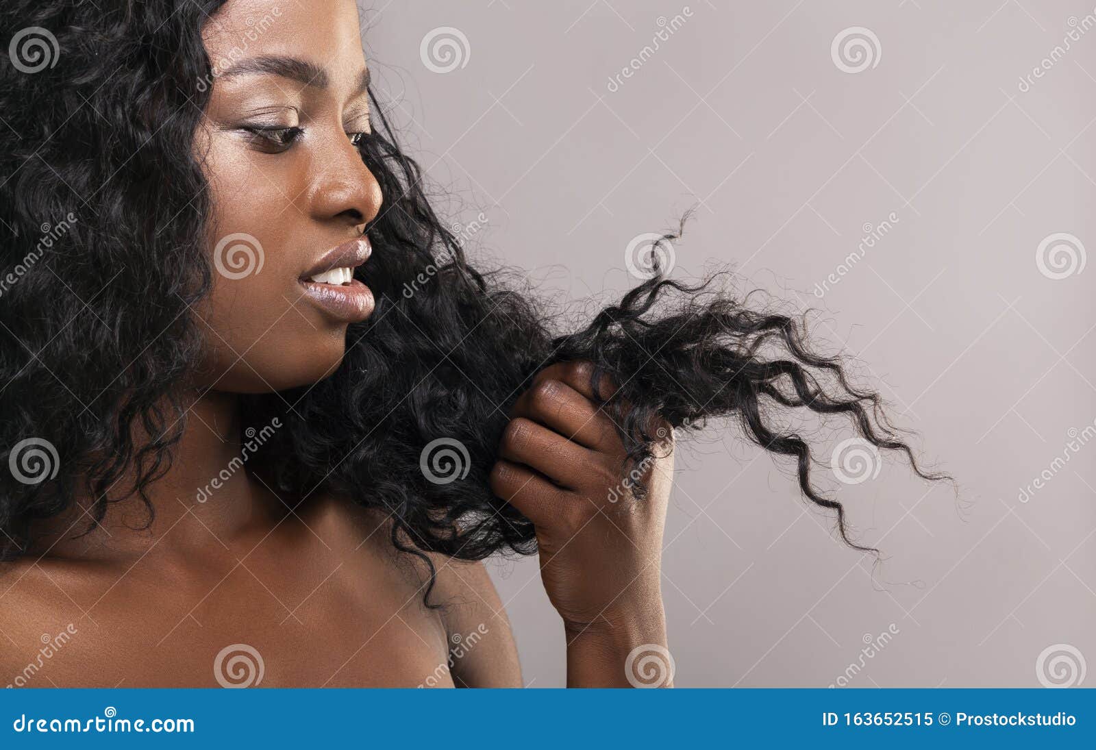 disappointed african american woman looking at her dry damaged hair