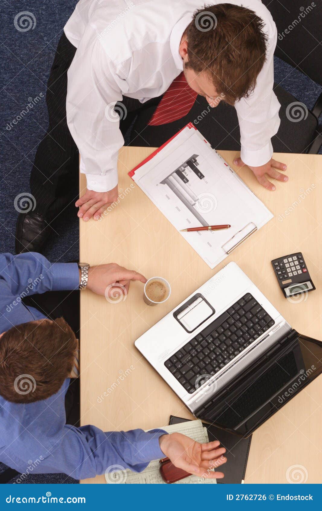 Diskussion Geschäft mit zwei Männern. Zwei junge Leitprogramme, die zusammen stationieren und den Inhalt eines Balkendiagramms behandeln und was auf einem Notebook-Computer gezeigt wird. Luftschuß genommen von direkt über der Tabelle.