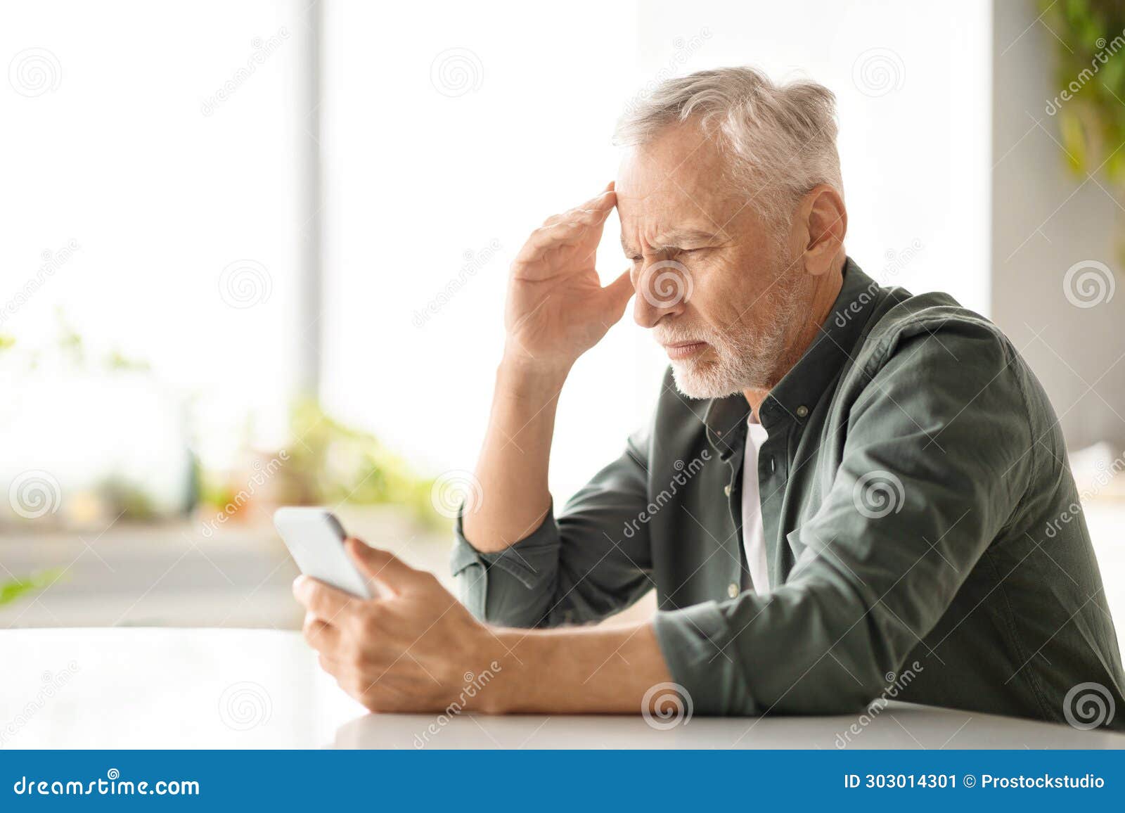 distressed elderly man suffering headache while looking at smartphone at home