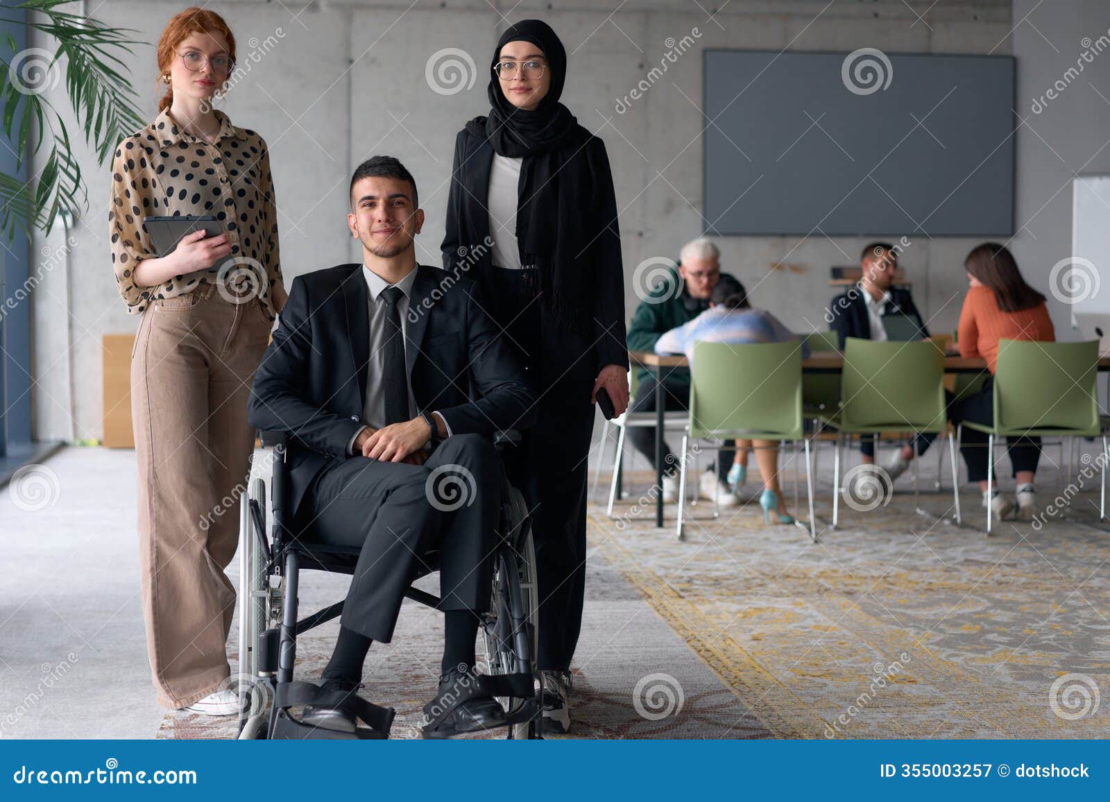 a diverse business team poses confidently, including a smiling director seated in a wheelchair, flanked by two