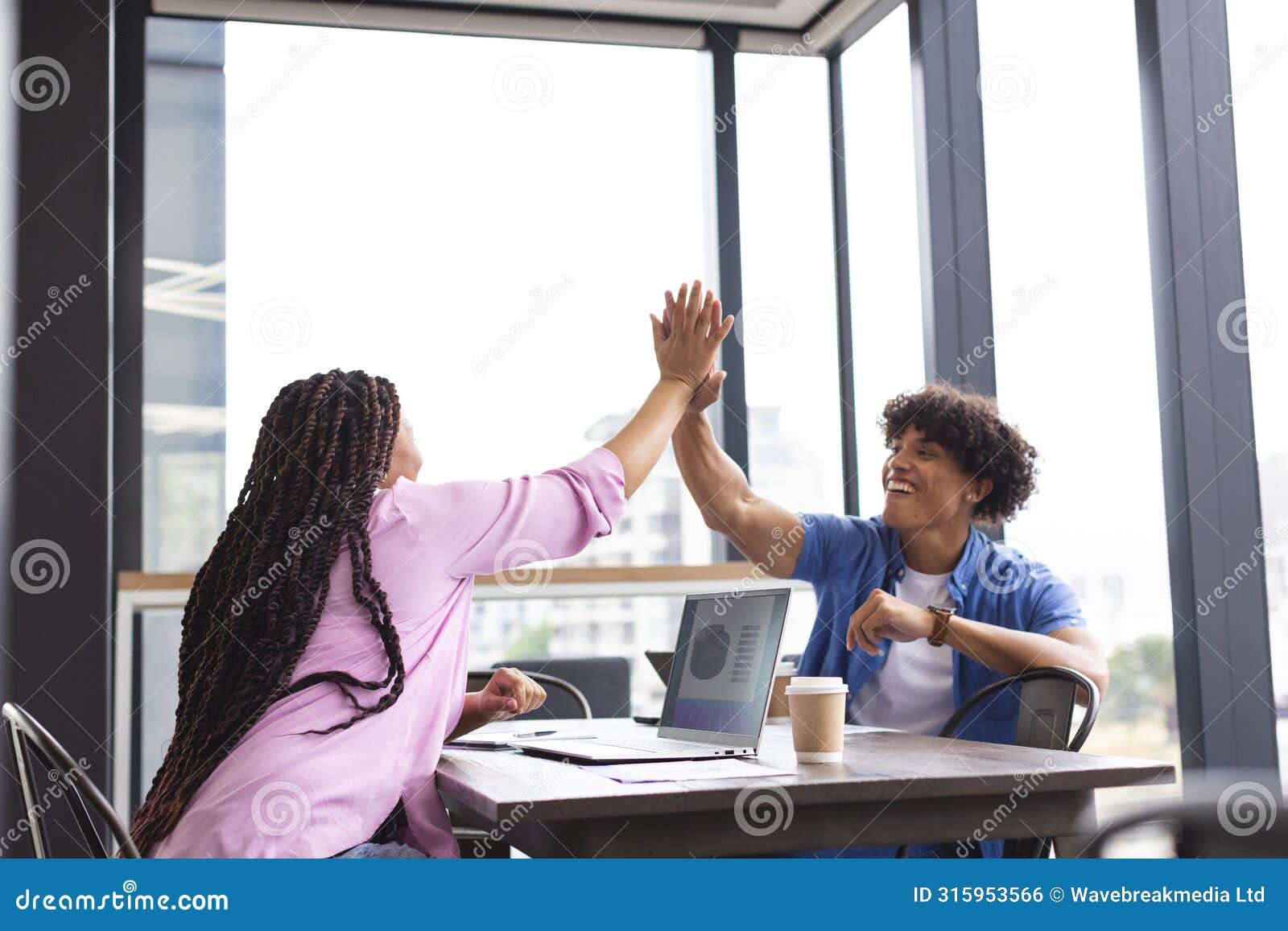 diverse colleagues high-fiving at table with a laptop in a modern business office
