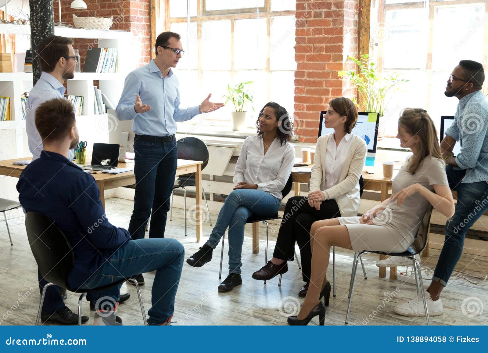 diverse employees listening to male manager speaking at group meeting