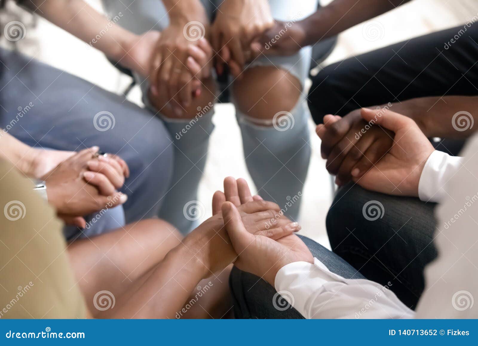 diverse people sitting in circle holding hands at group therapy
