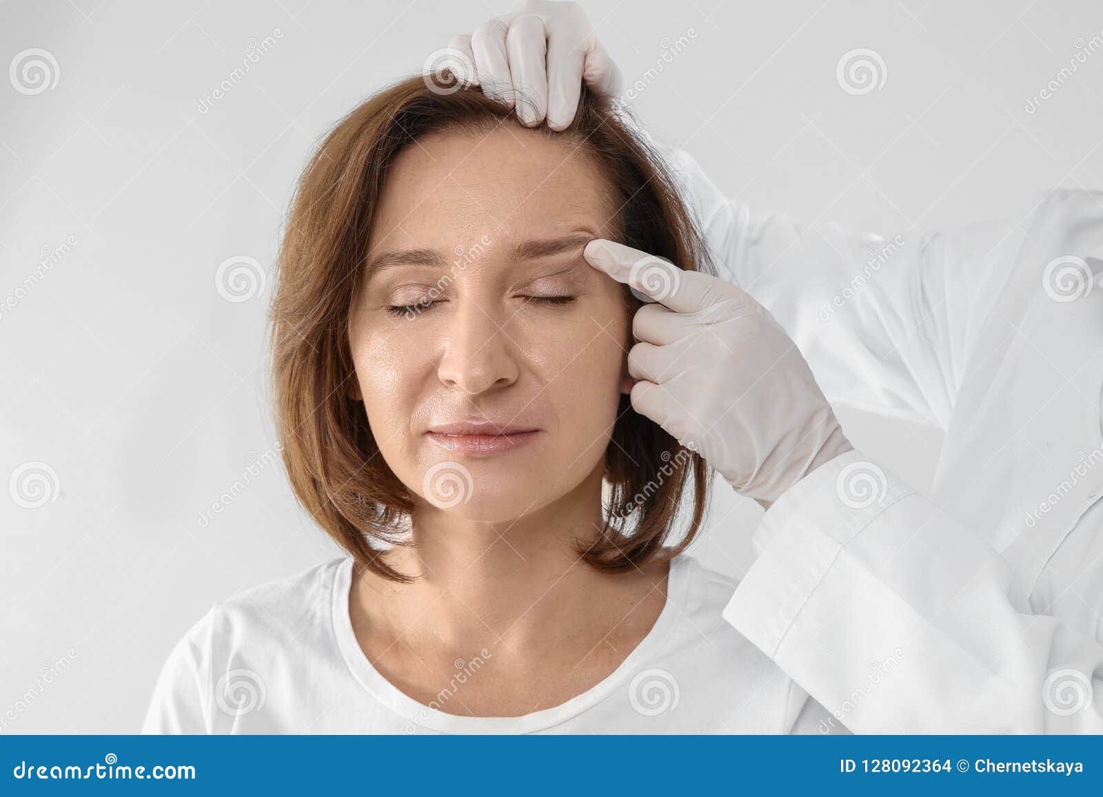 doctor examining mature woman face before surgery on white background